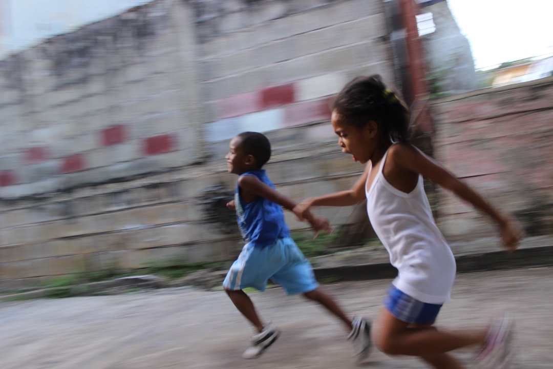 две девочки и мальчик бегут рядом с серой стеной